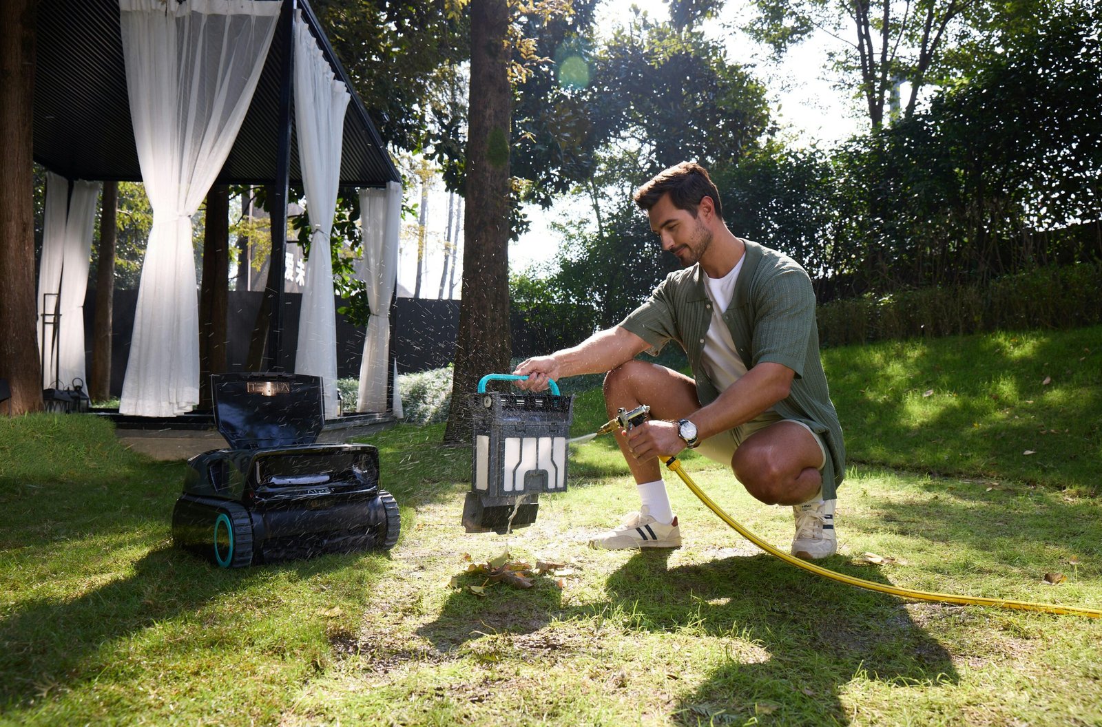 Man watering a robotic lawnmower in a garden.