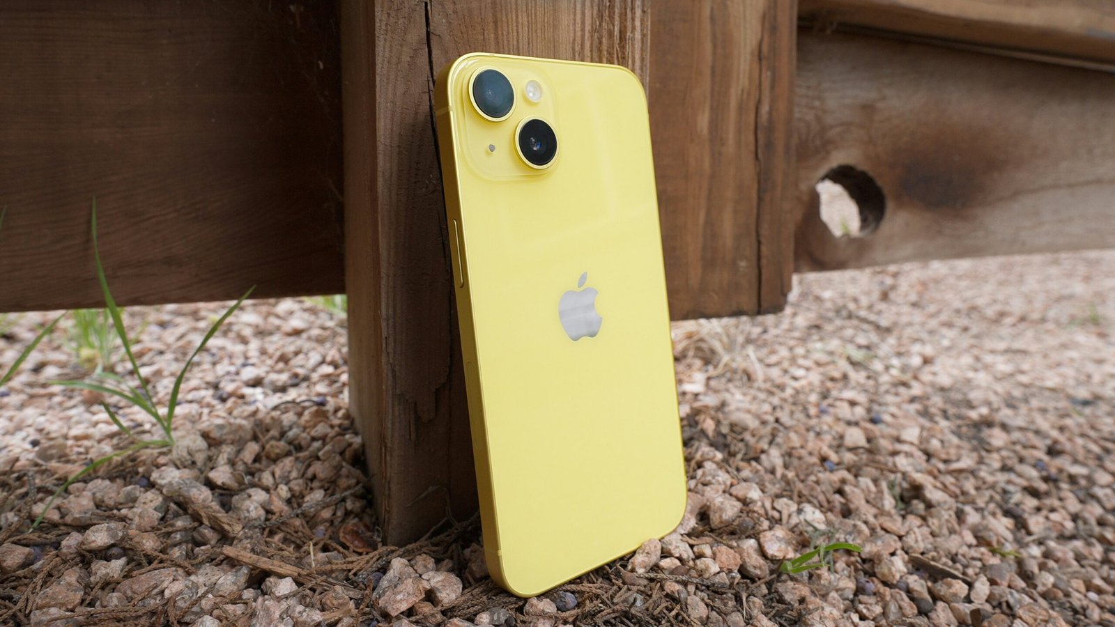 Yellow iPhone leaning against wooden post outdoors