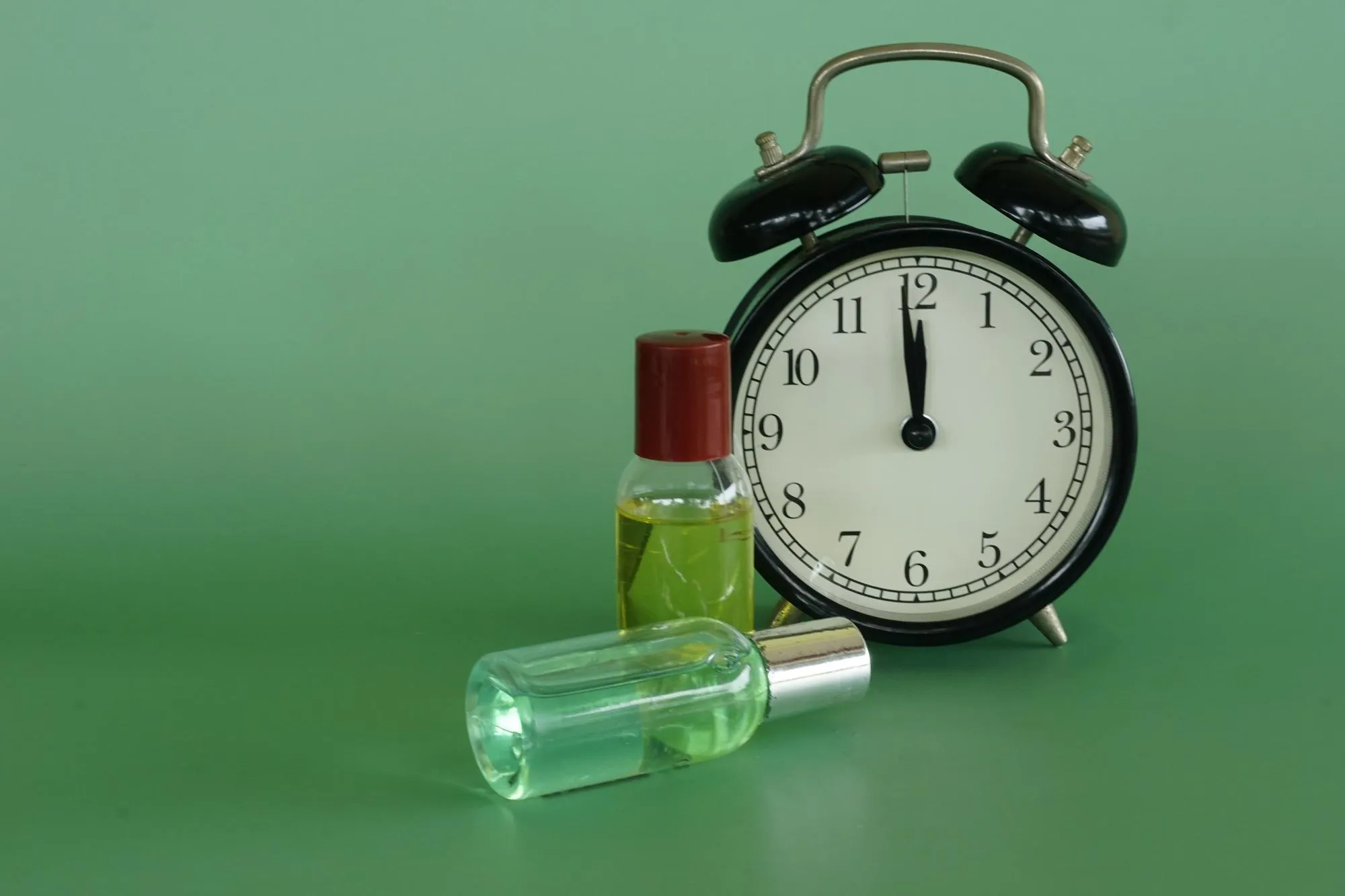 Alarm clock with body lotion bottles on the green background