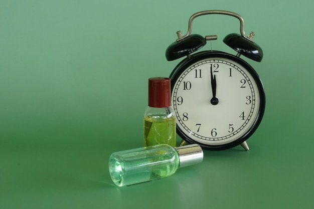 Alarm clock with body lotion bottles on the green background