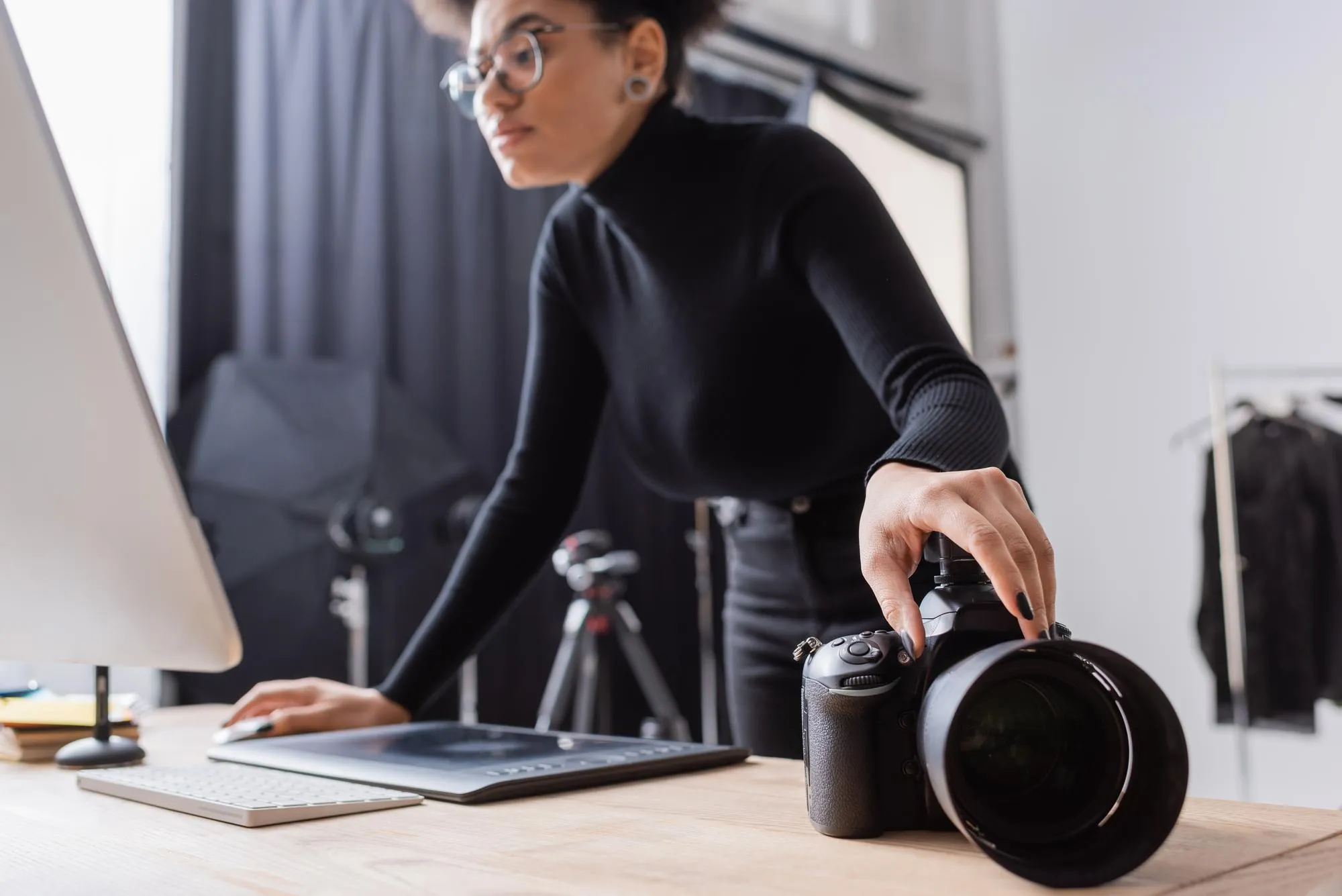 blurred african american content producer touching digital camera while looking at computer monitor