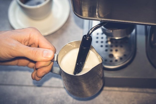 Cappuccino preparation Barista beating milk in milk seller Steamer Coffee machine Closeup