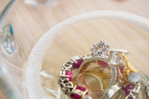 Cleaning vintage jewelry diamond ring and bracelet in glass on wood table background