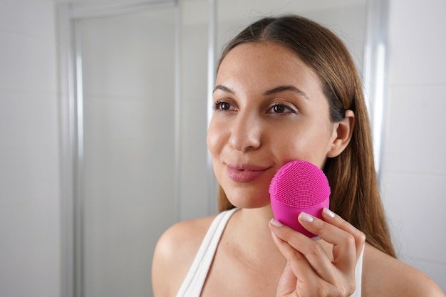 Close up of young woman cleaning skin with silicone brush ultrasonic vibrator in the bathroom
