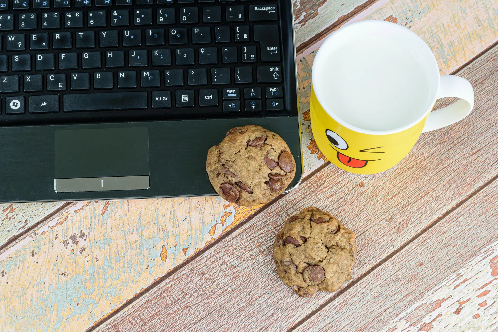 Cookies with drops of chocolate on the laptop, next to a yellow mug with milk, break for e-learning.