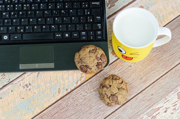 Cookies with drops of chocolate on the laptop, next to a yellow mug with milk, break for e-learning.