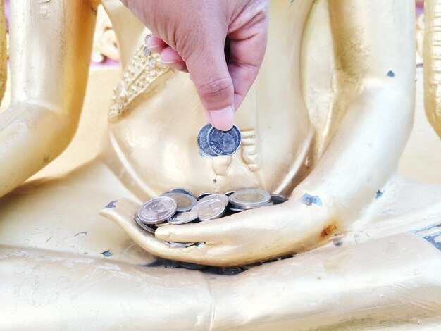 Cropped hand holding coins over statue