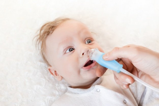 The doctor holds a tube in his hands to suck the snot from his nose. On the bed is a small child. Selective focus