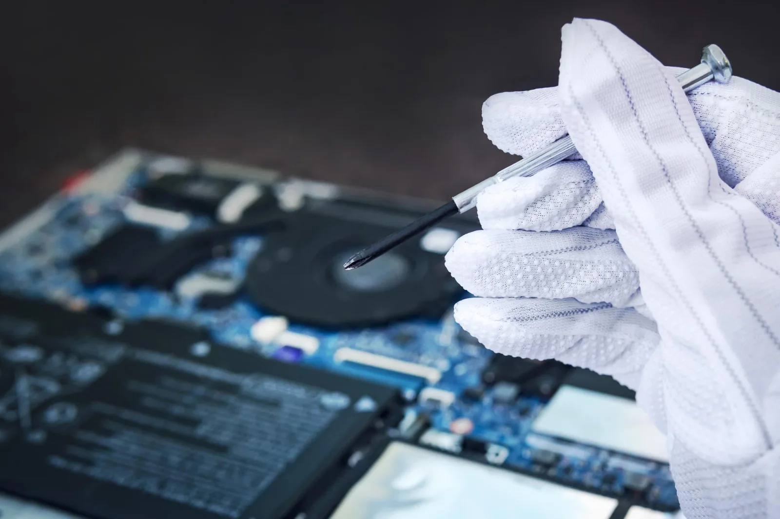 Engineer fixing broken computer at work IT technician repairing broken laptop notebook computer Computer Electronic repair shop concept hand in a white glove holds screwdriver hardware diagnostics