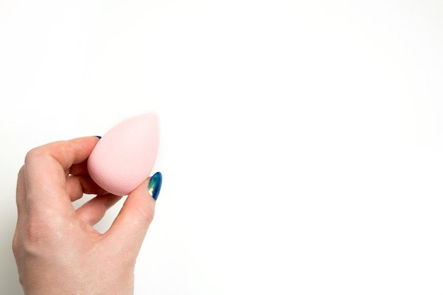 Female hand holding pink beauty blender over a white background. Space for text