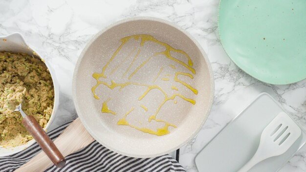 Flat lay. Step by step. Drizzling olive oil into the small frying pan to fry zucchini cakes.