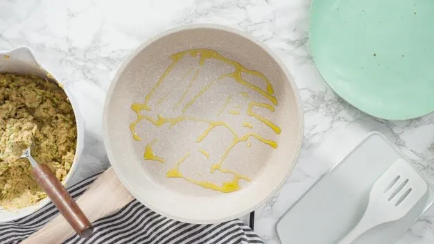 Flat lay. Step by step. Drizzling olive oil into the small frying pan to fry zucchini cakes.
