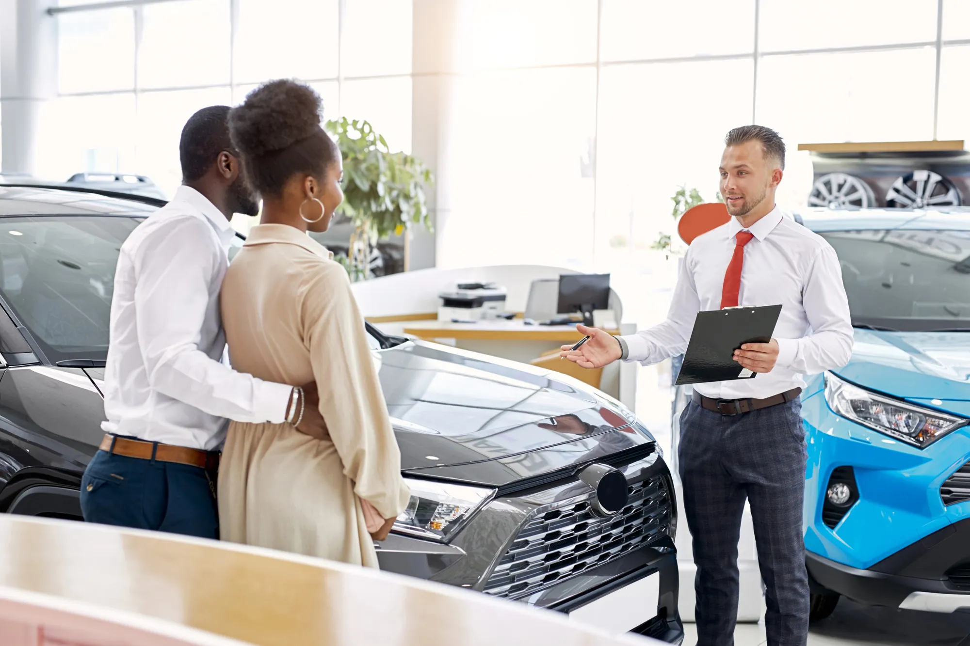 Friendly salesman and beautiful african couple in car showroom
