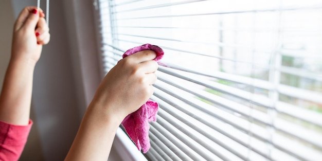 Hand of young woman cleaning blinds by a pink cloth housework cleaning concept