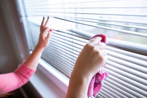 Hand of young woman cleaning blinds by pink cloth housework, cleaning woman