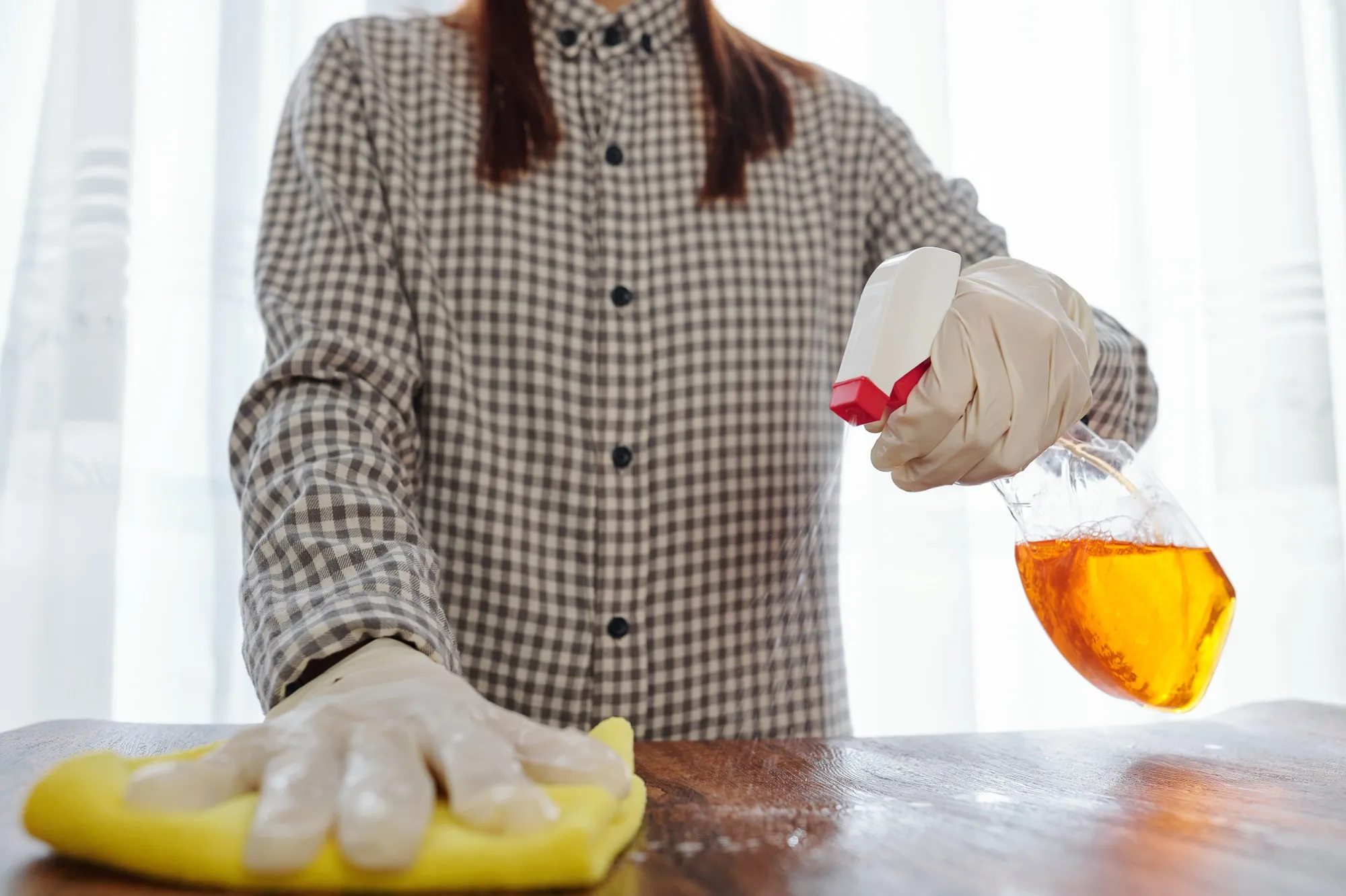 Housewife in latex gloves cleaning furniture surface with disinfecting spray