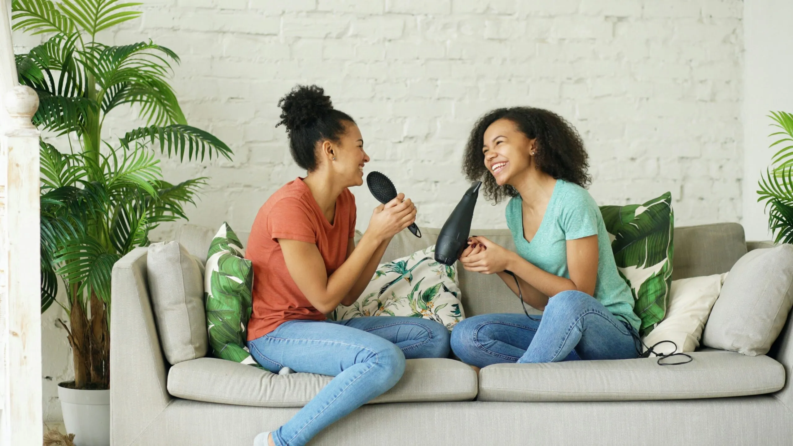 Two young women singing into hair dryers on couch