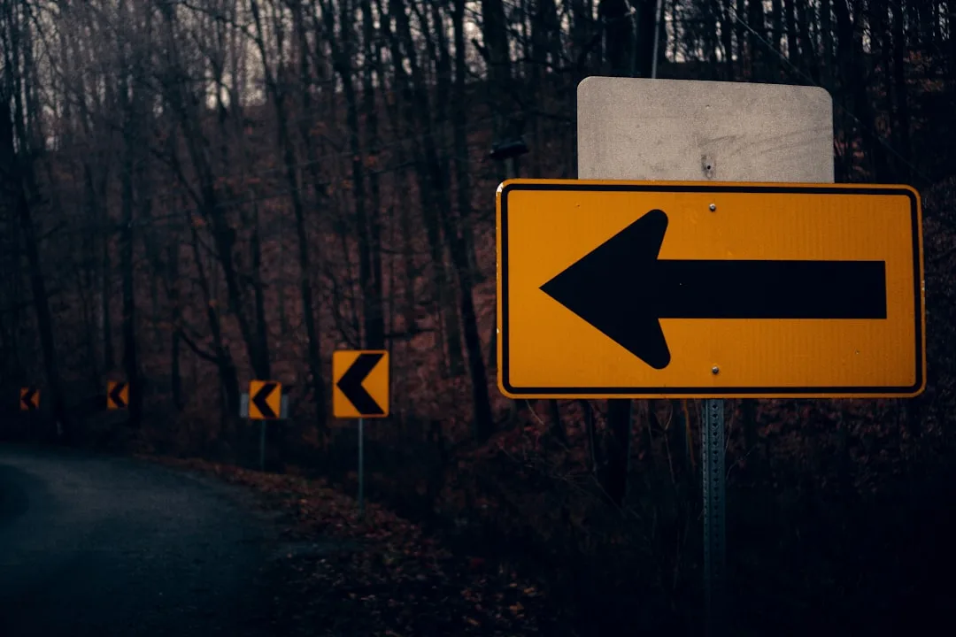 A yellow and black arrow sign and some trees