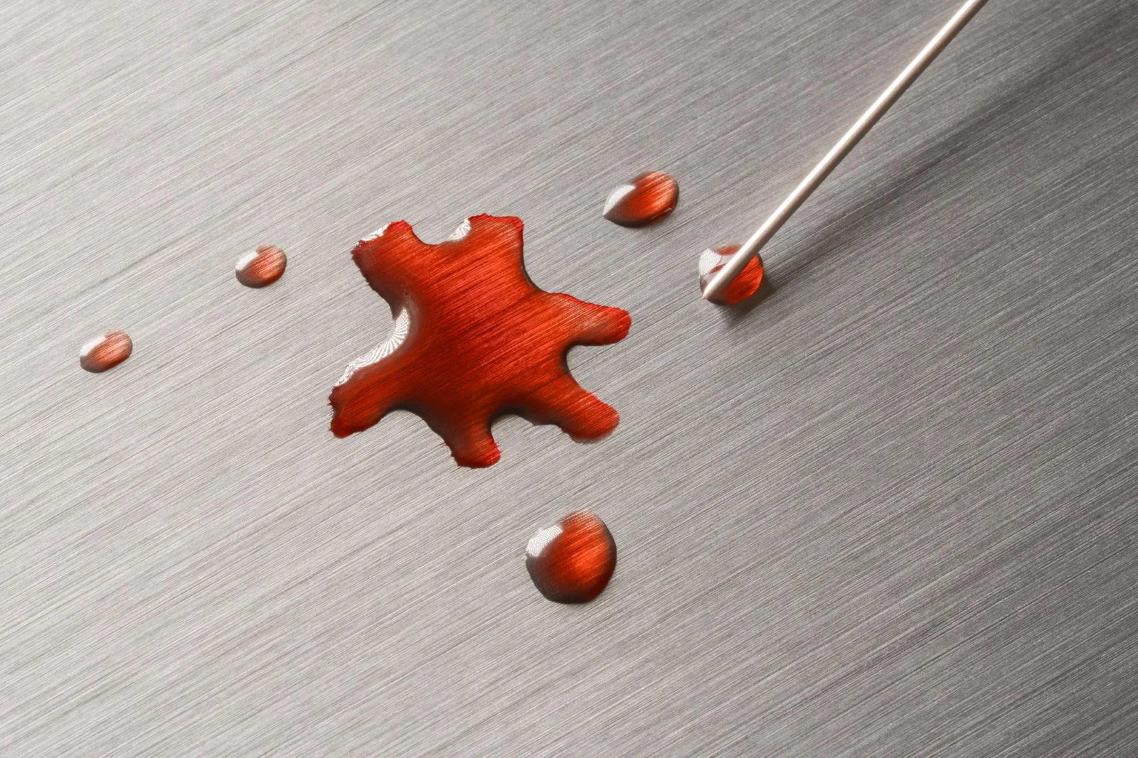 Liquid bloody blot on a metal surface surrounded by bloody drops painted needle