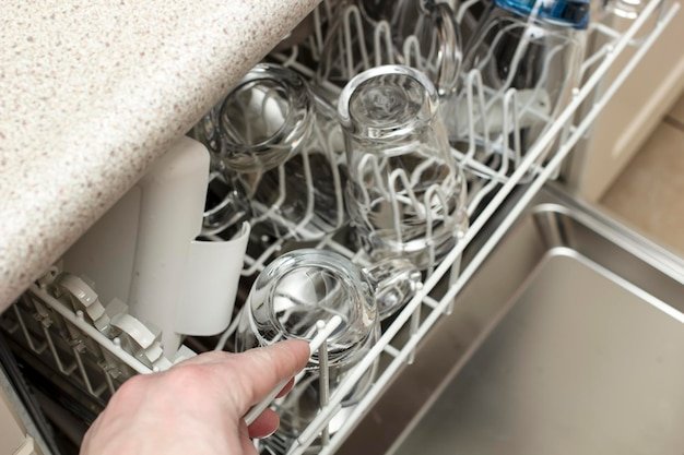 Man opened the dishwasher with his hand and was going to get perfectly clean dishes after washing.