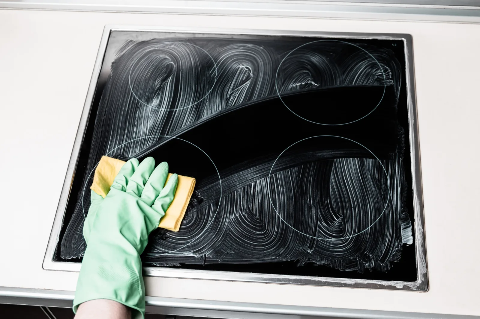 Man's hand in green glove cleaning cooker at home kitchen