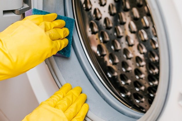 A man in yellow gloves cleans a dirty moldy rubber seal on a washing machine Mold dirt limescale in the washing machine Periodic maintenance of household appliances