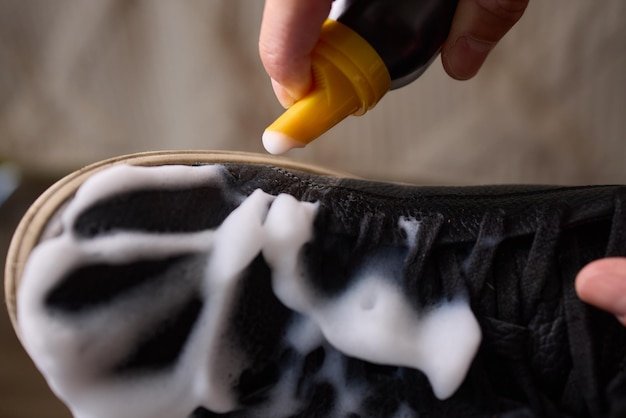 A person is scrubbing a shoe with a sponge and foamy cleaner