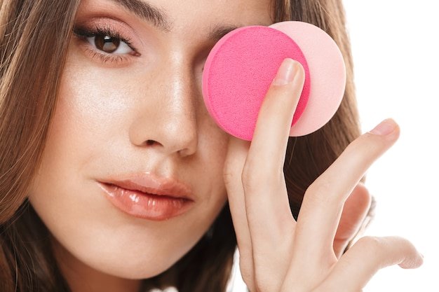 Portrait closeup of attractive young woman applying cosmetics with makeup sponges