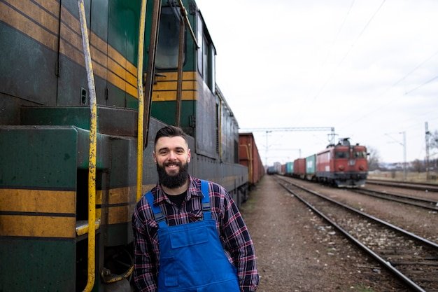 Portrait of engine train driver standing by locomotive at train station ready for departure.