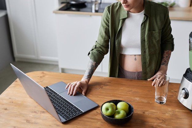 Pregnant young woman using laptop in kitchen interior checking work messages