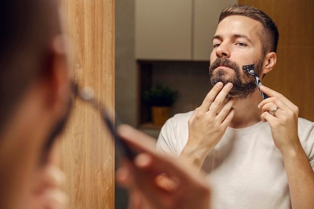 Reflection of a man shaving his beard with razor blade