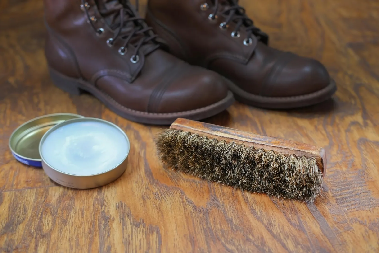 shoe cream and brush on wooden floor against leather boots, cleaning and brushing shoes