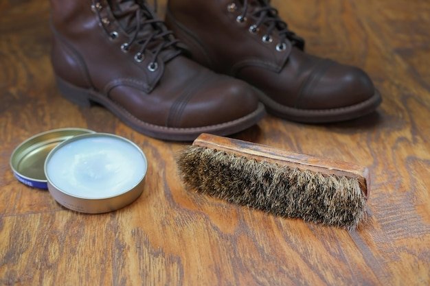 shoe cream and brush on wooden floor against leather boots, cleaning and brushing shoes