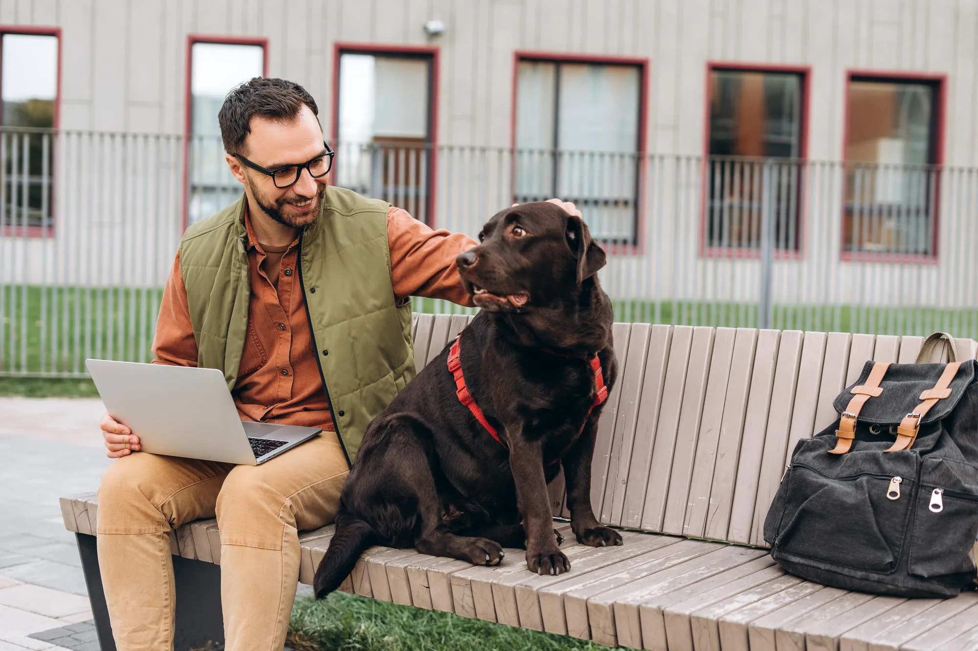 Smiling happy Hispanic man freelancer using laptop petting beautiful black dog labrador