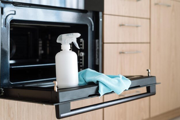 Spray bottle with detergent and cleaning cloth on open oven door