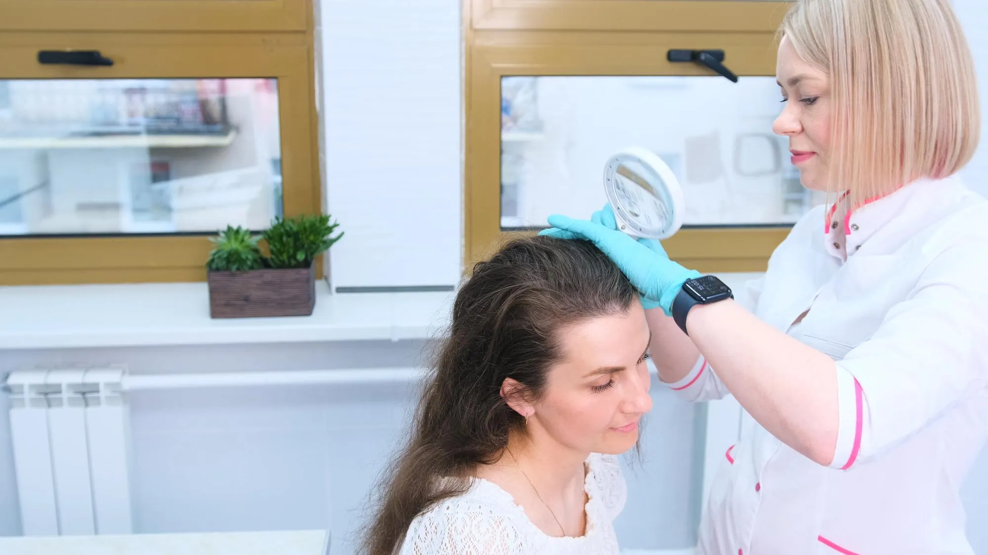 A trichologist examines the condition of the hair on the patient's head using a lens