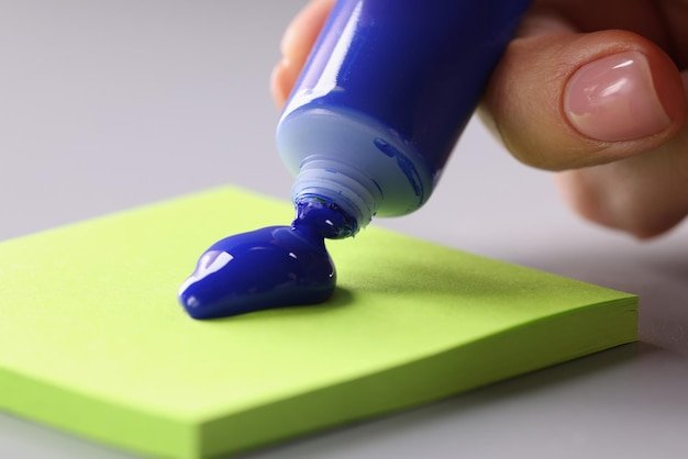 Tube of blue acrylic paint drips onto colored sticker