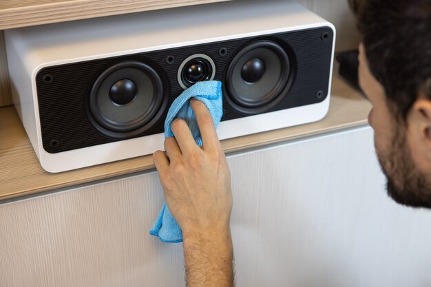An unrecognizable Caucasian man does a wet cleaning, dusting a musical speaker system. Spring cleaning concept, hygiene in the house, changing roles in the family. Soft selective focus.