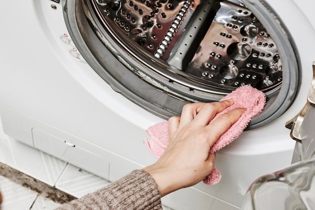 An unrecognizable woman cleans the washing machine