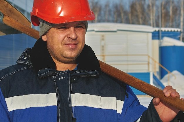 White man in a helmet overalls and with a shovel Portrait of a worker in the winter