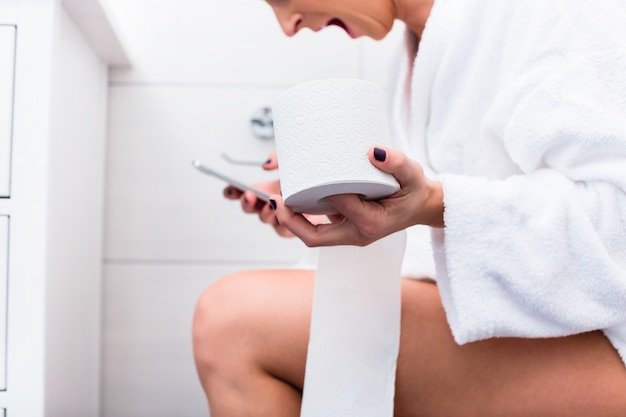 Woman sitting on toilet writing text message on cell phone
