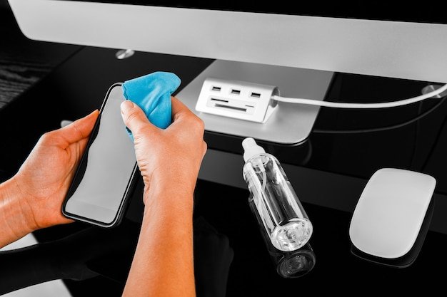 Woman Wiping Mobile Phone Screen With Sanitizer on wood background. Cleaning smart phone screen to prevent corona virus Covid 19