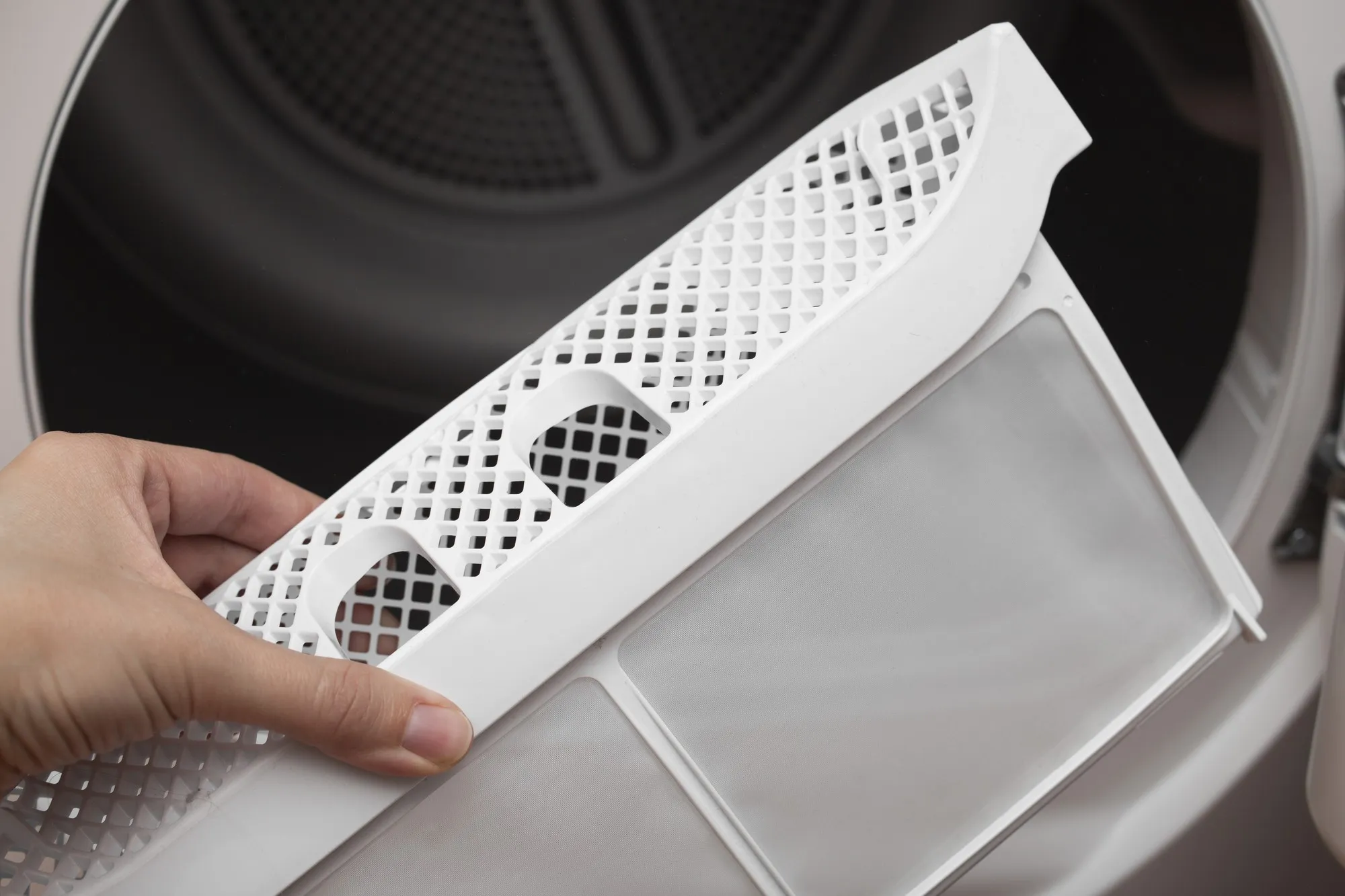 A womans hand takes out the filter of the drying machine down filter for clothes dryers removing fluff from the dirty air filter of the dryer after using the machine