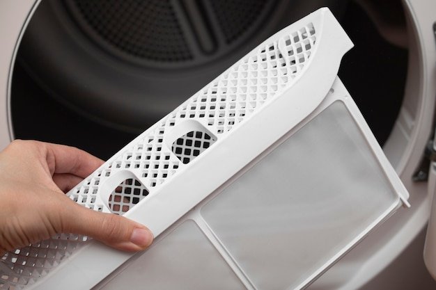 A womans hand takes out the filter of the drying machine down filter for clothes dryers removing fluff from the dirty air filter of the dryer after using the machine