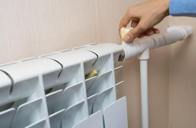 A womans hand turns a thermostat on a battery a battery a home heater in a room Heating season