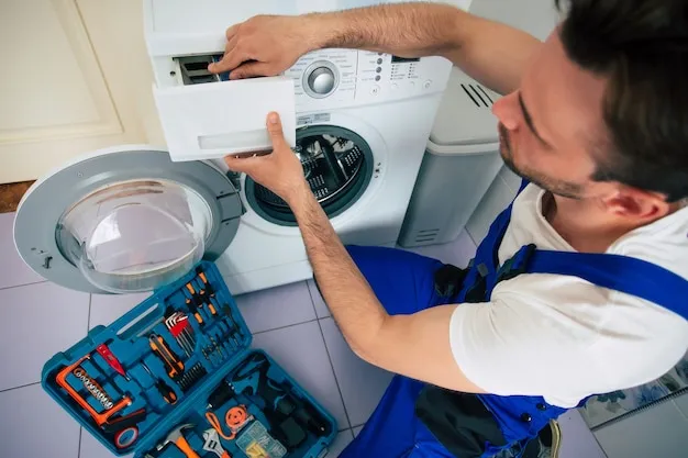 The young handsome repairman in worker suit with the professional tools box is fixing the washing machine in the bathroom