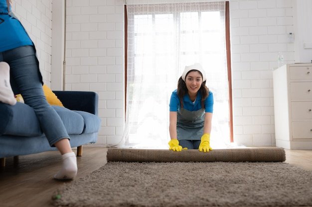 Young women cleaning maid in uniform and rubber gloves are cleaning the room fold up carpet