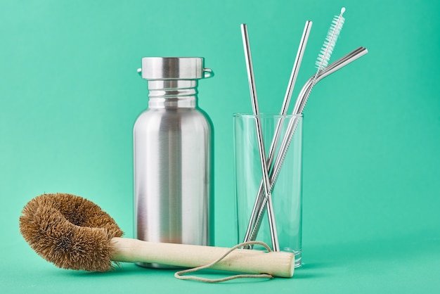 Zero waste concept. Eco friendly reusable items aluminum bottle and metal tubes in glass on green wall