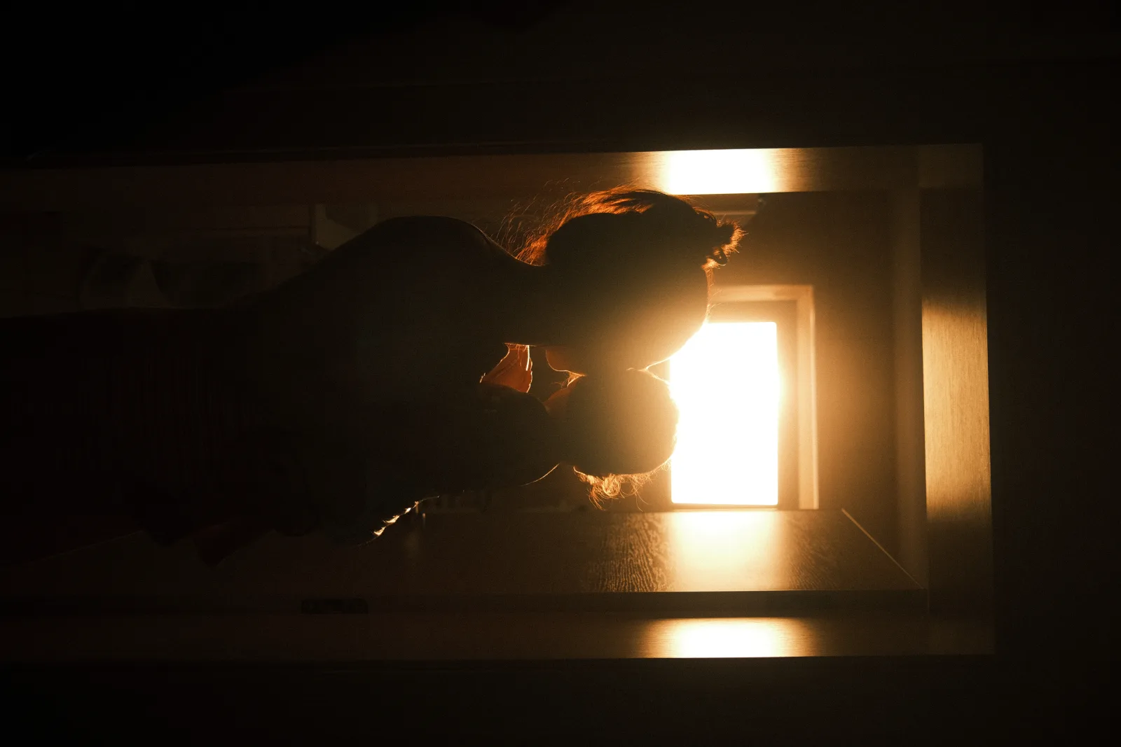 A mother embraces her child in a softly lit doorway as the warm light from the setting sun casts a beautiful silhouette. The moment captures love and tenderness.