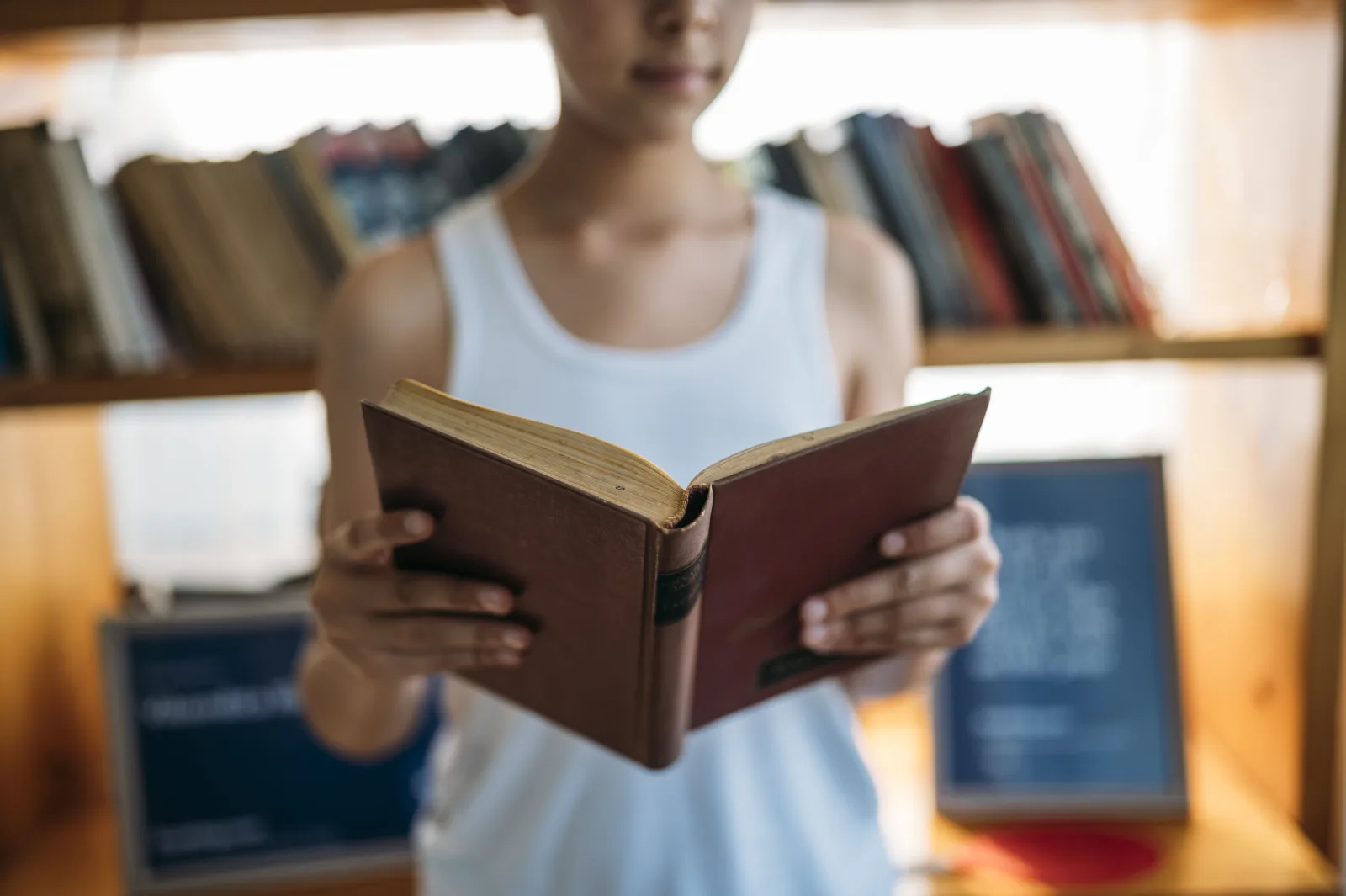 Young person reading a book in a cozy library surrounded by shelves of literature